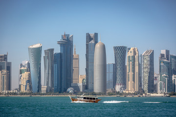 The skyline of Doha with a traditional boat in the foreground in Qatar, on a blue sky day, winter time, seen from the MIA Park