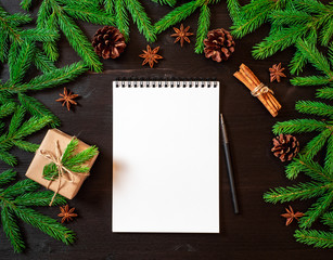 Wall Mural - Empty white notebook and pen on dark black Christmas background of fir branches, cones, gifts. Letter, mock up