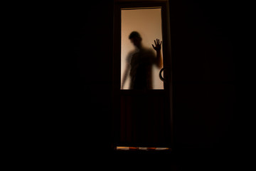 Silhouette of an unknown shadow figure on a door through a closed glass door. The silhouette of a human in front of a window at night. Scary scene halloween concept