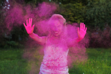 Happy caucasian girl with curly hair posing in a cloud of pink dry paint, celebrating Holi festival