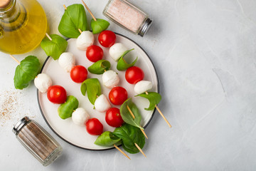 Caprese salad - skewer with tomato, mozzarella and basil, italian food and healthy vegetarian diet concept on a light background. Top view with copy space. Flat lay