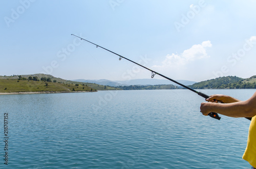 Fotografía Unrecognizable man holding fishing rod next to beautiful lake on beautiful sunny