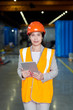 © Seventyfour - Portrait of female factory worker wearing hardhat and reflective vest looking at camera and smiling cheerfully while posing in workshop of production plant, copy space