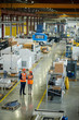 © Seventyfour - High angle full length portrait of bearded businessman wearing hardhat inspecting production workshop accompanied by smiling young woman, copy space