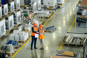 Wall Mural - High angle full length portrait of bearded businessman wearing hardhat inspecting production workshop accompanied by female factory worker, copy space