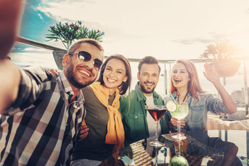 Nice shot. Group of cheerful friends taking photo while sitting at the table with cocktails