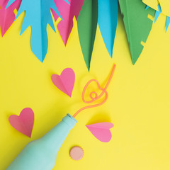 Wall Mural - Painted in blue beer or cocktail bottle lies on a yellow background among hearts and palm tropical leaves made of paper. Summer party concept