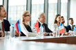 © pressmaster - Row of foreign participants in political summit sitting by long table with their flags in front