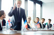 © pressmaster - Aged confident politician in suit standing by table and debating with his foreign colleagues at political event