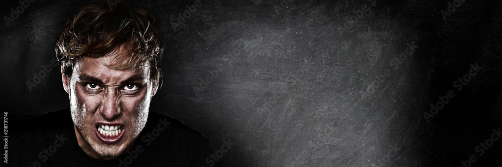 Angry agressive man face ready to fight on blackboard chalk board black texture background panoramic banner for advertising. Scary upset athlete focused to win.