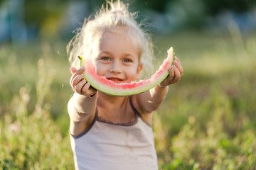 Little blond girl eating watermelon in the park.