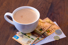 Closeup Of A Cup Of Coffe With A Bill And Kazakhstani Tenge Banknotes And Coins On A Dark Wooden Table