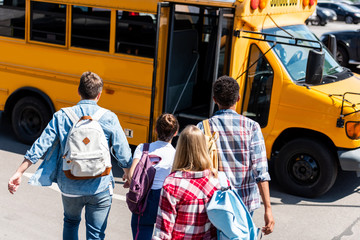 rear view of group of teen students walking to school bus after school