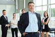 © opolja - Mature smiling business manager crossing his arms in front of his business team.