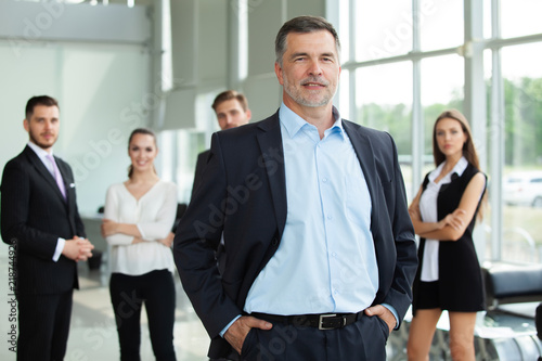 Fotomural Mature smiling business manager crossing his arms in front of his business team