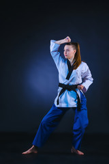 The karate girl in white kimono and black belt training karate over gray background.