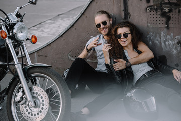 Canvas Print - smiling couple of bikers embracing and smoking on asphalt with chopper motorcycle