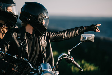 Canvas Print - couple of bikers in helmets on motorcycle, man pointing at something