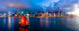 Panorama of Hong Kong City skyline with tourist sailboat at night. View from across Victoria Harbor HongKong.