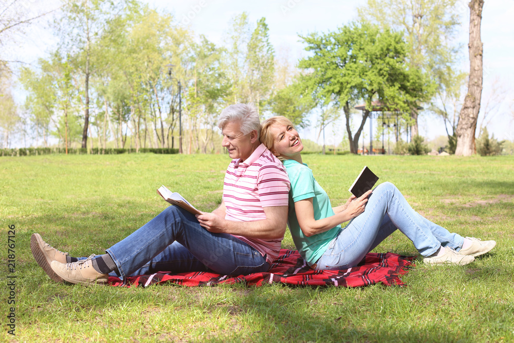 Mature couple reading books in park on spring day