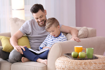 Wall Mural - Father and his son reading book together at home