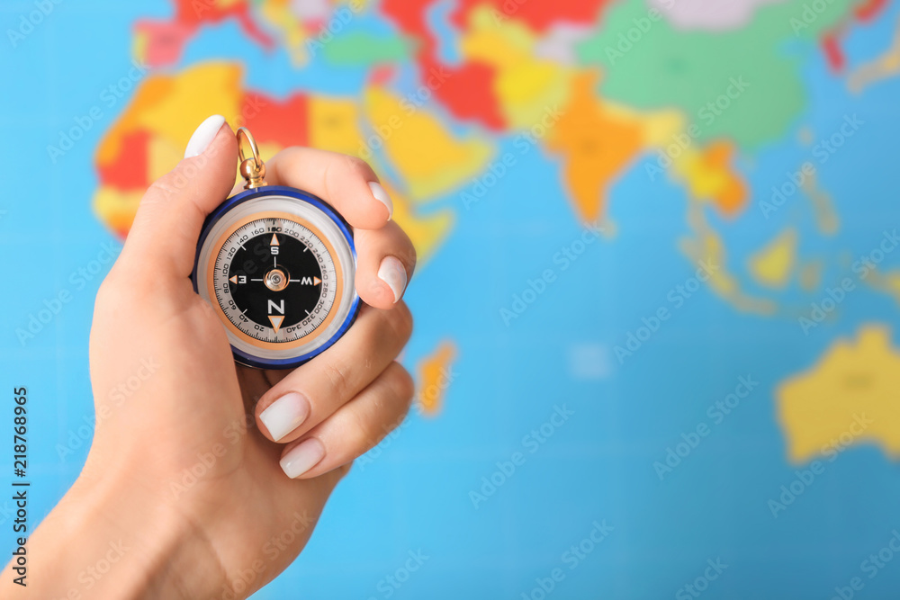 Woman holding modern compass against blurred world map, closeup