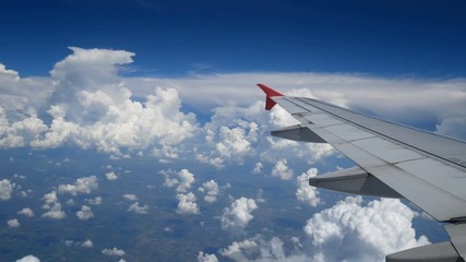 Wall Mural - 4K footage airplane flight. wing of an airplane flying above the white clouds and blue sky. beautiful aerial view from the window of the plane on travelling time by aircraft. holiday , vacation time