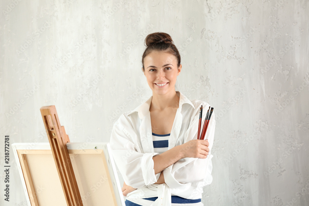 Female artist with brushes and easel on grey background
