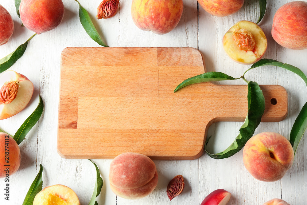 Board and fresh peaches on white wooden table