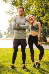 Wall Mural - Photo of happy young people man and woman 20s in sportswear, training together in green park during sunny summer day