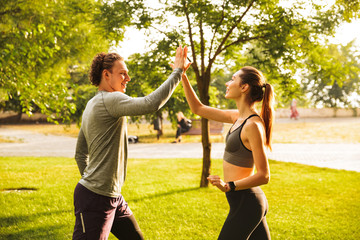 Poster - Photo of happy young man and woman 20s in tracksuits, doing workout together in green park during sunny summer day