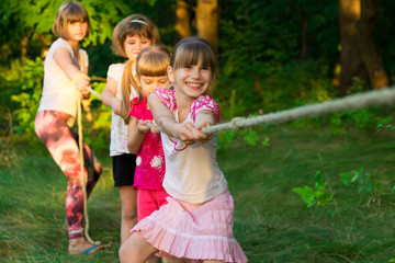 Wall Mural - Group of happy children playing tug of war outside on grass. Kids pulling rope at park. Summer camp fun