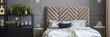Bed with headboard between gold tables in grey bedroom interior with plants. Real photo