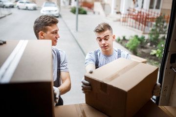 Wall Mural - Two young handsome movers wearing uniforms are unloading the van