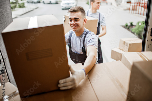 Fotografiet A young handsome smiling mover wearing uniform is reaching for t