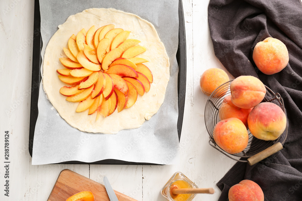 Baking tray with raw peach galette and fresh fruit on table