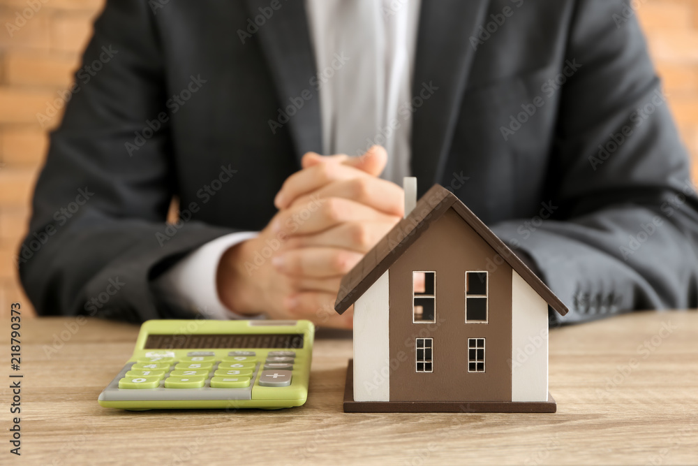 Man with house model and calculator at wooden table. Mortgage concept