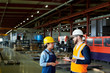 © Seventyfour - Side view portrait of production manager wearing hardhat talking to female factory worker standing in production workshop, copy space
