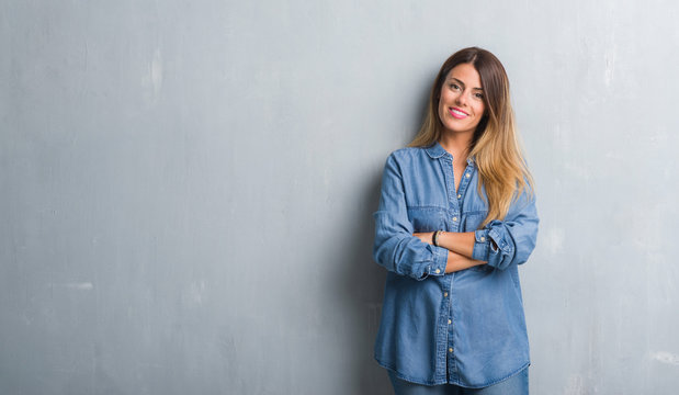 Young adult woman over grunge grey wall wearing denim outfit happy face smiling with crossed arms looking at the camera. Positive person.