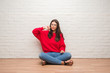 © Krakenimages.com - Young brunette woman sitting on the floor over white brick wall with angry face, negative sign showing dislike with thumbs down, rejection concept