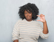 © Krakenimages.com - Young african american plus size woman over grey grunge wall wearing a sweater smiling and confident gesturing with hand doing size sign with fingers while looking and the camera. Measure concept.