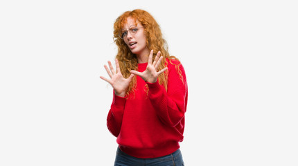 Canvas Print - Young redhead woman wearing red sweater afraid and terrified with fear expression stop gesture with hands, shouting in shock. Panic concept.