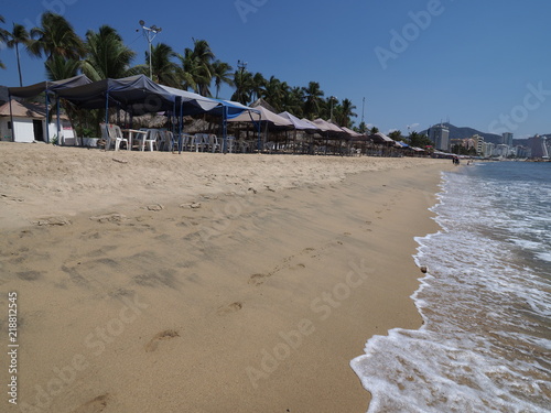Fotografering Umbrellas and exotic palms on brilliant sandy beach at bay of Acapulco city land