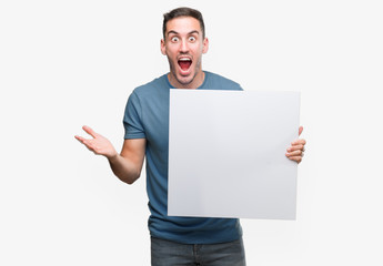 Sticker - Handsome young man holding advertising banner very happy and excited, winner expression celebrating victory screaming with big smile and raised hands