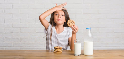 Canvas Print - Young hispanic kid sitting on the table drinking milk and eating chocolate cooky stressed with hand on head, shocked with shame and surprise face, angry and frustrated. Fear and upset for mistake.