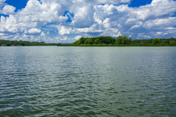 Wall Mural - A beautiful image of landscape from the center of the river, surrounded by trees and reeds on the shore and distant horizon against the blue sky in clouds. Reflection, water, tourist destination