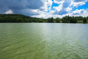 Wall Mural - A beautiful image of landscape from the center of the river, surrounded by trees and reeds on the shore and distant horizon against the blue sky in clouds. Reflection, water, tourist destination