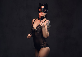 Sexy woman wearing black lingerie in BDSM cat leather mask and accessories posing on dark background. 