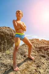 cute little boy in swimming trunk climbing rocks on the stony beach