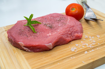 raw beef steak on cutting board with cherry tomatoes and basil leaf